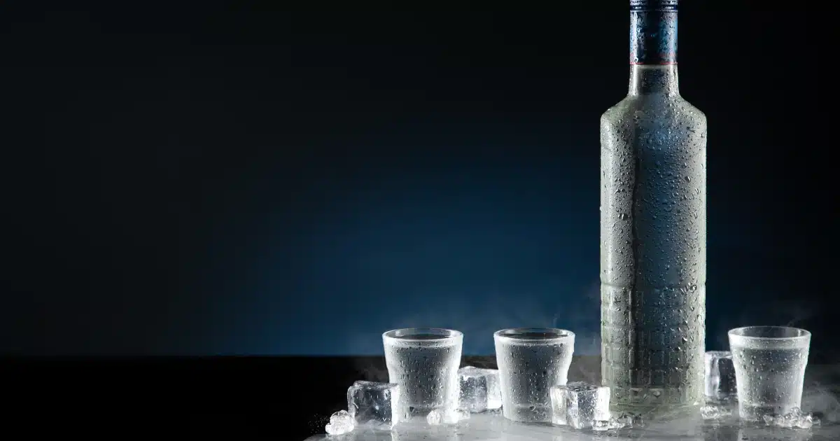 Ice-cold bottle of vodka with shot glasses on dark blue background